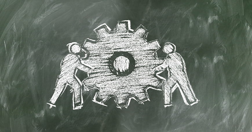 Chalk drawing of teamwork pushing a gear on blackboard