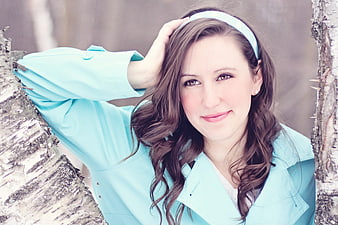 Smiling Brunette Woman In Turquoise Coat Leaning Against Birch Tree