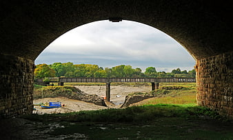 View of dry riverbed and railway bridge through stone arch
