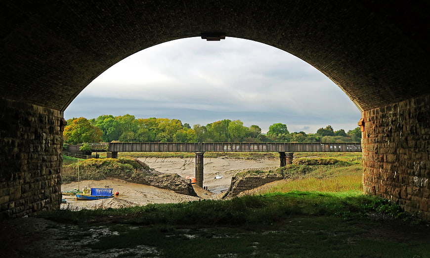 View of dry riverbed and railway bridge through stone arch