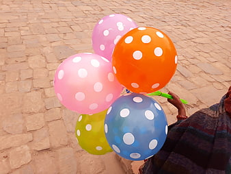 Hand holding colorful polka dot balloons on cobblestone street