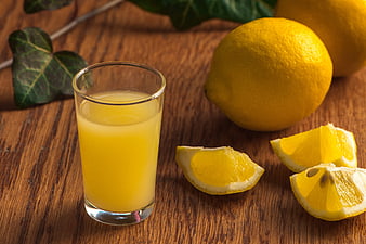 Fresh lemon juice in glass with lemons on wooden table