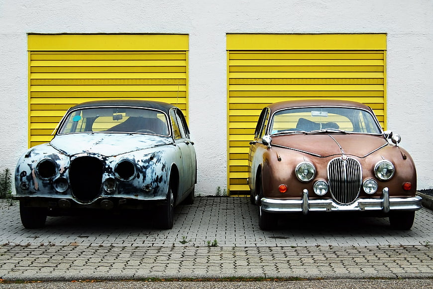 Two vintage Jaguar cars parked in front of yellow garage doors