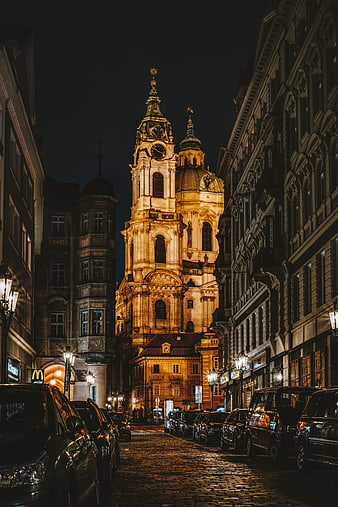 Illuminated Baroque Church Tower on Cobblestone Street in Prague at Night