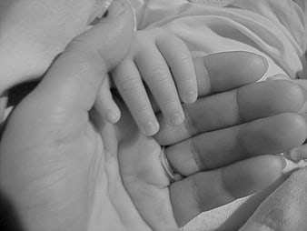 Black and white close-up of a mother's hand holding a baby's hand