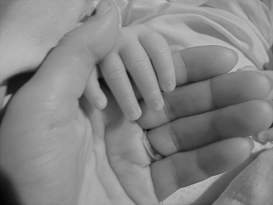 Black and white close-up of a mother's hand holding a baby's hand