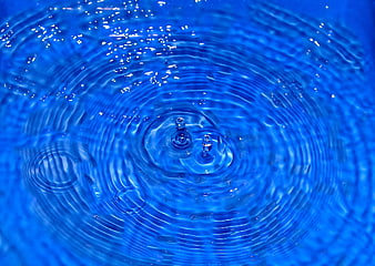 Blue water droplet creating concentric ripples and splashes
