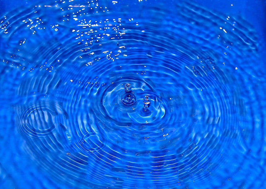 Blue water droplet creating concentric ripples and splashes