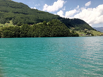 Turquoise alpine lake with green forested mountains and blue sky