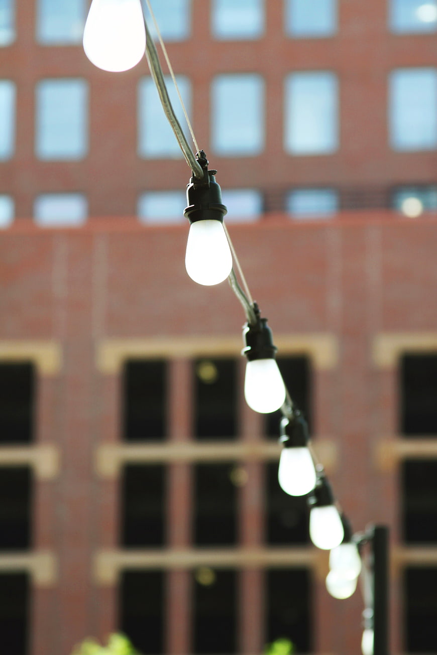 String of glowing light bulbs against blurred brick building