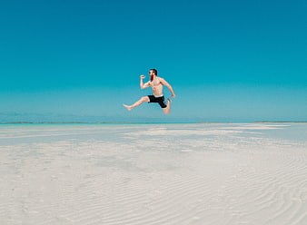 Man Jumping on White Sand Beach with Blue Sky