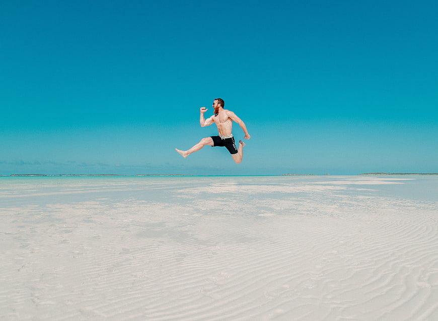 Man Jumping on White Sand Beach with Blue Sky