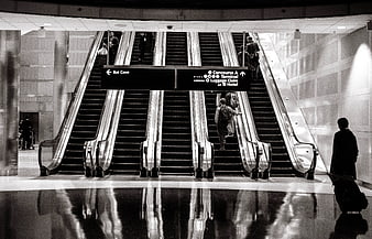 Black and white airport escalators with travelers and directional signs