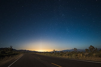 Desert Highway Under Starry Night Sky with Distant City Glow