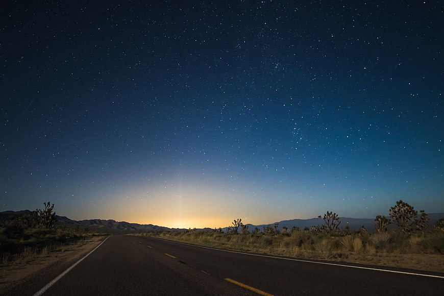 Desert Highway Under Starry Night Sky with Distant City Glow