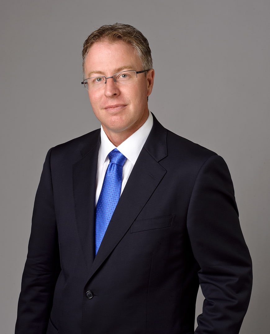 Professional corporate portrait of a man in a dark suit and blue tie
