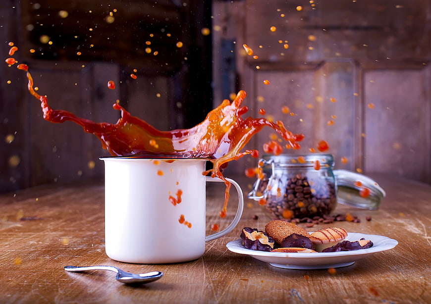 Dynamic coffee splash in white enamel mug with cookies
