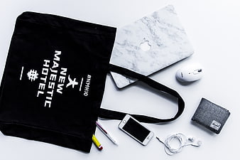 Flat lay of black tote bag, marble laptop, and tech accessories