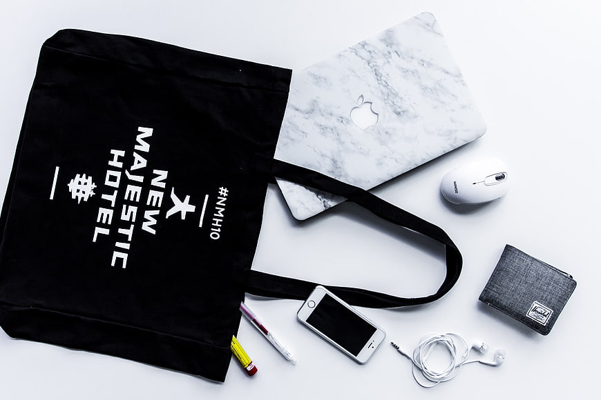 Flat lay of black tote bag, marble laptop, and tech accessories