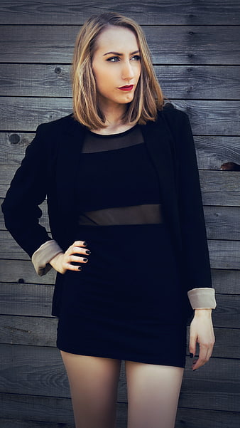 Confident blonde woman in black dress against wooden wall