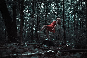Woman in red dress floating in dark forest with surreal levitation effect