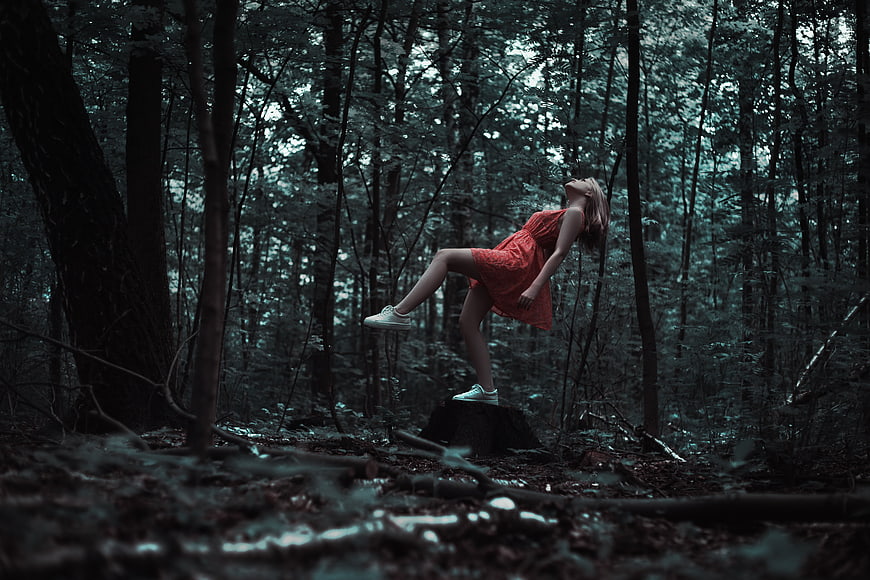 Woman in red dress floating in dark forest with surreal levitation effect