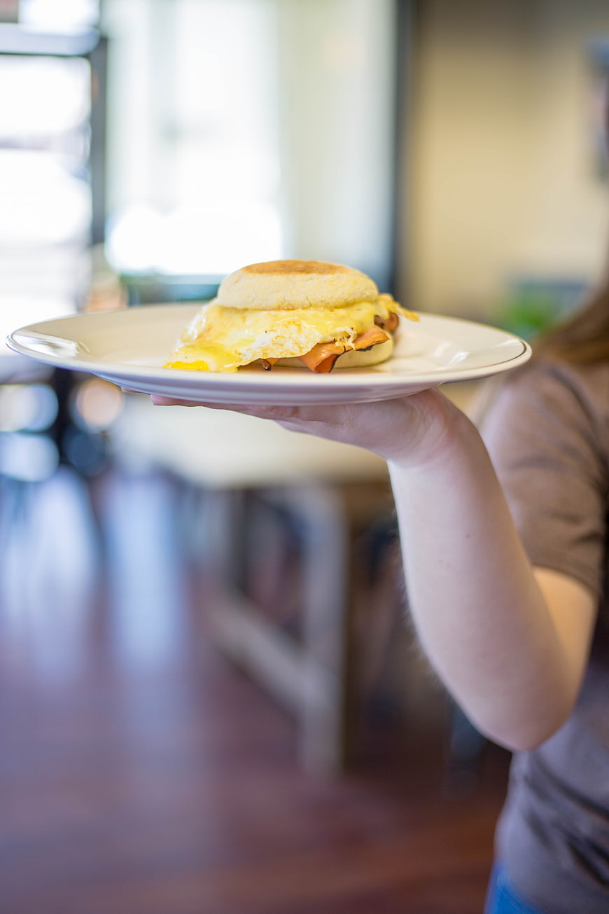 Waitress Holding English Muffin Breakfast Sandwich on White Plate