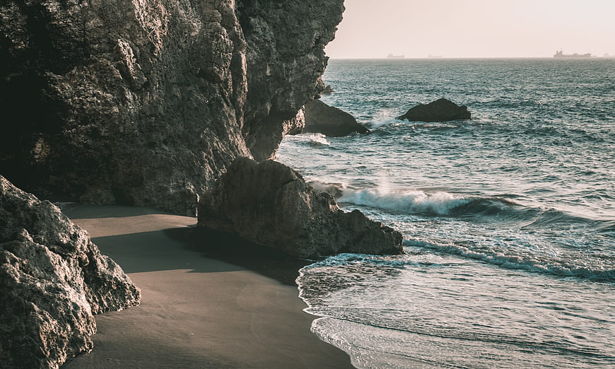 Secluded rocky cove with gentle waves and distant ships