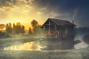 Rustic wooden cabin by a lake at sunrise with morning mist