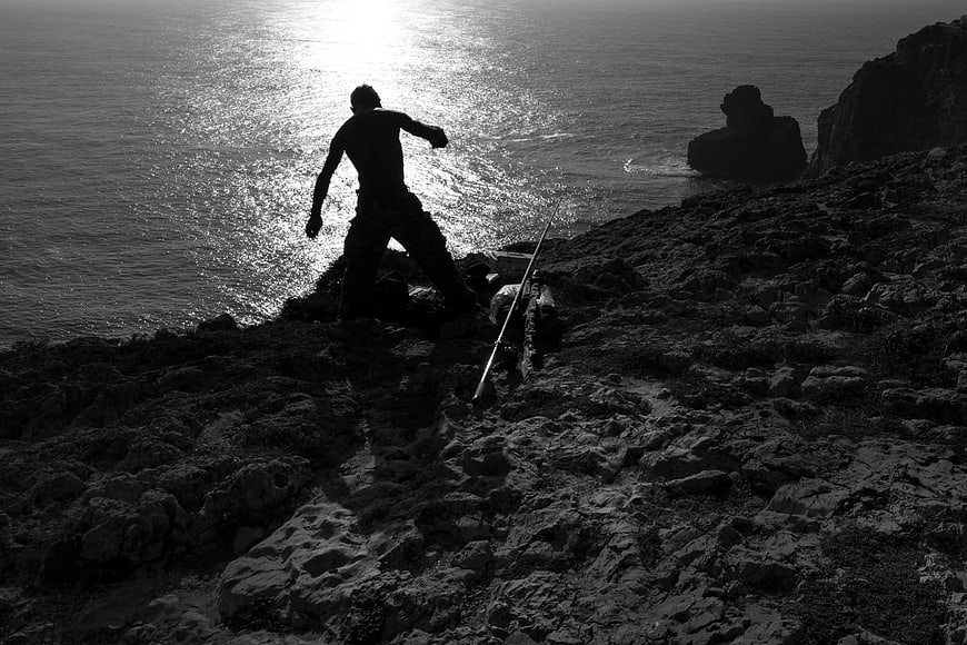 Silhouette of Man Standing on Rocky Cliff by Ocean