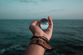 Hand holding crystal ball over ocean horizon