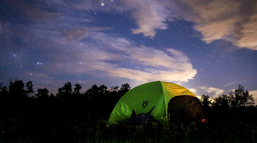 Green camping tent under starry night sky with clouds