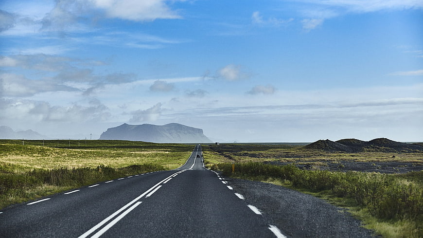 Empty asphalt road stretching to distant mountains under blue sky
