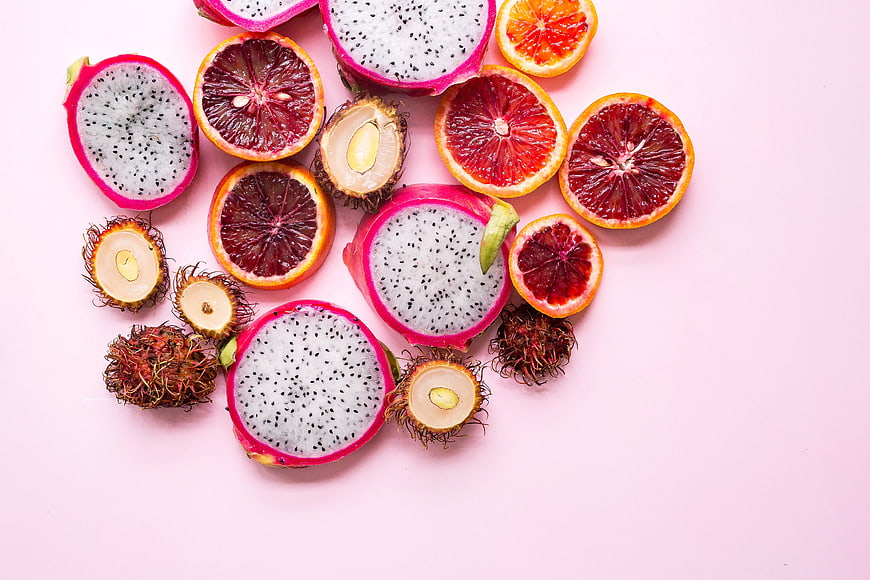 Sliced Dragon Fruit, Blood Oranges, and Rambutan on Pink Background