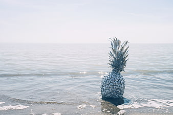 Surreal silver pineapple standing in ocean waves on beach