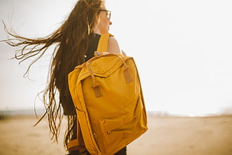Woman with Yellow Backpack Walking on Sandy Beach