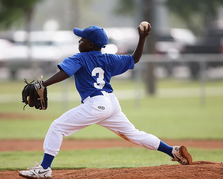 Young Baseball Pitcher in Blue Jersey Throwing Ball