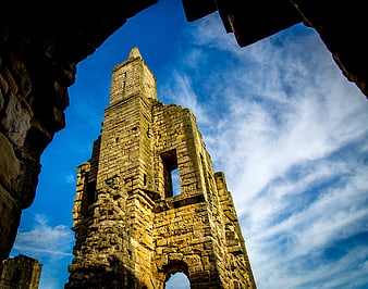 Low angle view of Warkworth Castle ruins against blue sky