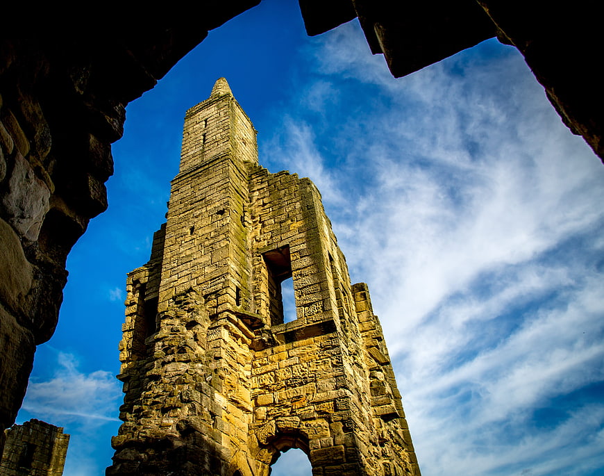 Low angle view of Warkworth Castle ruins against blue sky