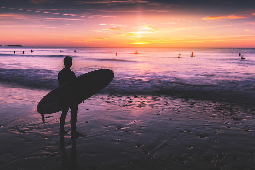 Silhouette of a surfer holding a board on a beach at sunset
