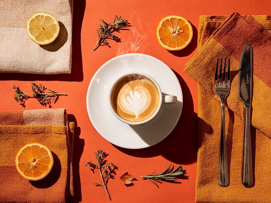 Flat Lay of Latte with Citrus Slices and Herbs on Orange Background