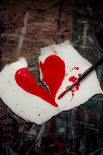 Broken red heart painted on torn paper with brush on rustic wooden table