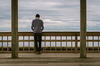 Man Standing Alone on Wooden Deck Overlooking Ocean