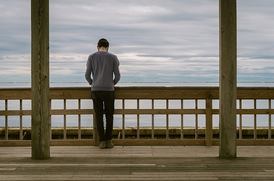 Man Standing Alone on Wooden Deck Overlooking Ocean