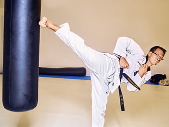 Male martial artist performing high kick on heavy bag in gym