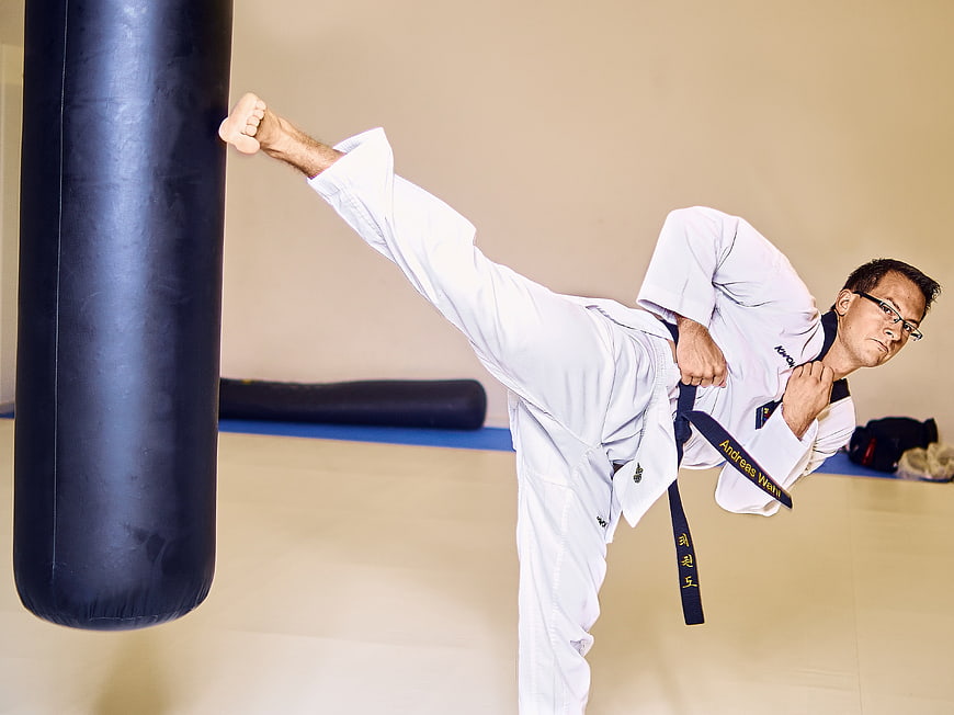 Male martial artist performing high kick on heavy bag in gym