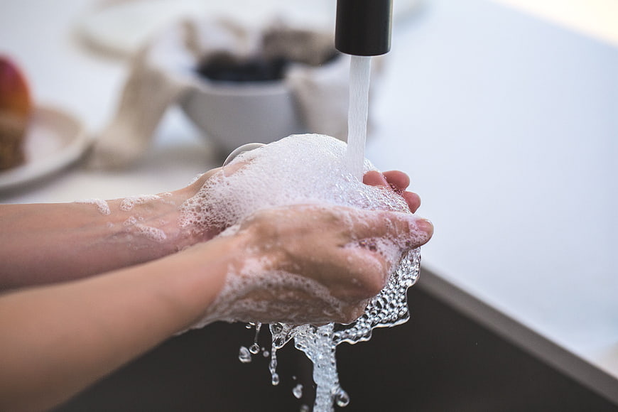 Close-up of hands washing with soap and water under faucet