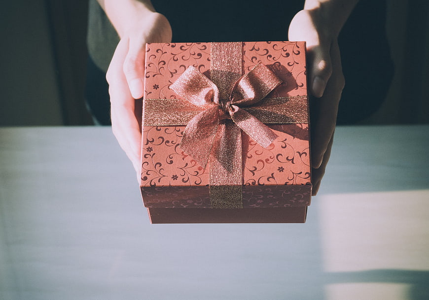 Hands holding a pink gift box with a gold ribbon bow