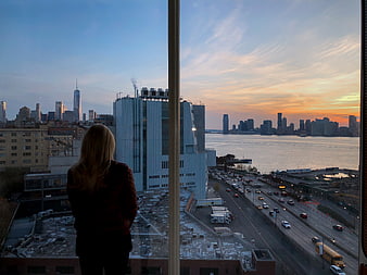 Woman Looking Out Window at City Skyline Sunset