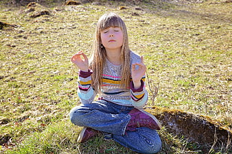 Young girl meditating in a grassy field outdoors